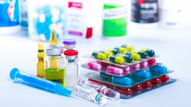 Pillen, Spritzen und Medikamentenschachteln liegen auf einer weißen Oberfläche gestapelt.