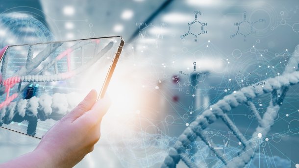 Zwei Hände, die ein Tablet halten und Projektion von DNA-Strängen im Hintergrund.