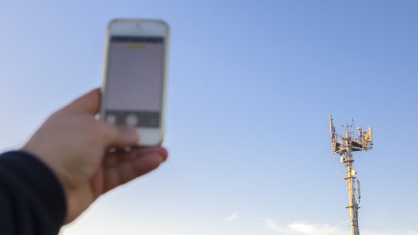 Man holds cell phone in front of cell tower