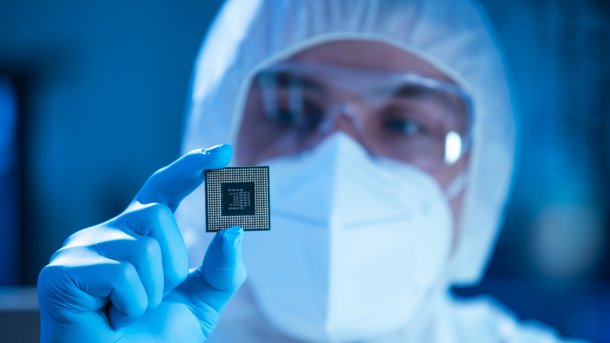 Eine Person in Reinraumkleidung hält einen Computerchip in die Kamera