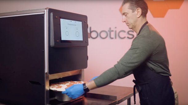 Mann entnimmt Pizza aus Pizza-Roboter.