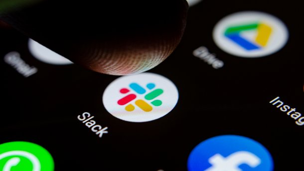 Close-up of a smartphone display, in the center the symbol of the Slack app with a finger hovering over it.