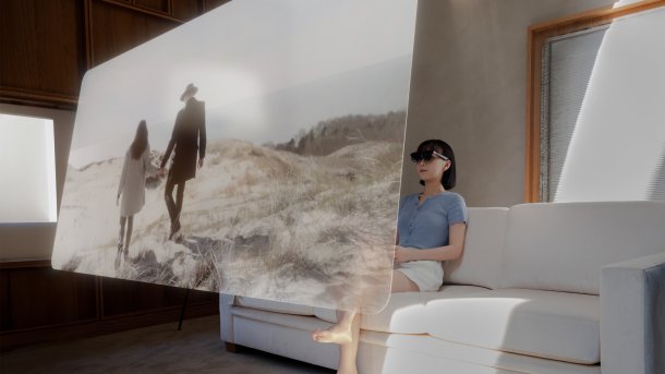 Eine Frau sitzt auf einem Sofa mit einer Display-Brille und blickt auf eine virtuelle Leinwand, die vor ihr im Raum schwebt.