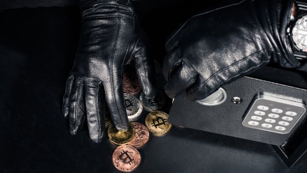 Hände in schwarzen Handschuhe greifen nach Bitcoin-Münzen neben einem Safe