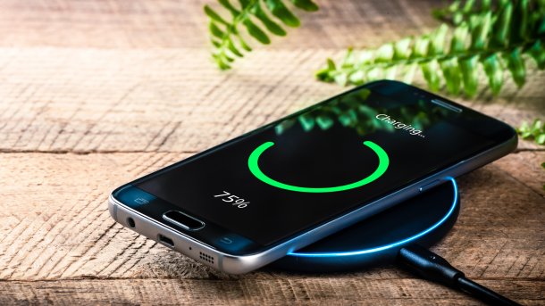A smartphone is lying on a table on a wireless charger and is being charged. The display shows that it is three-quarters charged.