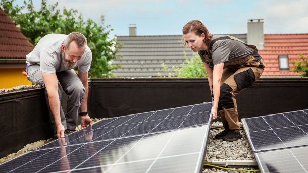 A woman and a man install a solar panel on a roof 
