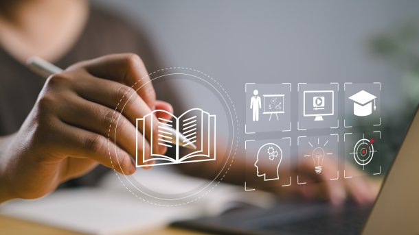A primary school pupil with glasses sits in a classroom with other children and reads something on a laptop.