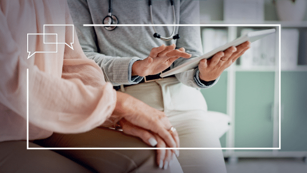 Eine Person hält ein Tablet, daneben eine ältere Person mit einer rosa Bluse.