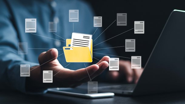 Eine Person sitzt am Laptop. Davor ein Symbol für einen offenen Ordner. Drumherum verschiedene Dateien, ebenfalls als Symbole. 