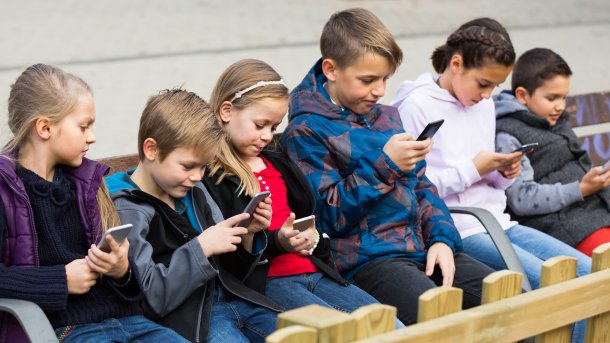 Kinder auf einer Bank, alle gucken auf ihr Smartphone