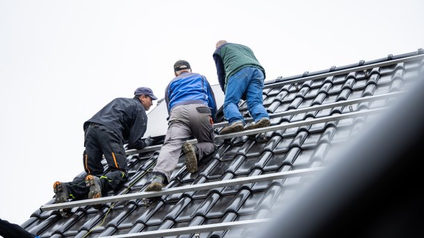 Drei Männer arbeiten auf einem schwarzen Dach.
