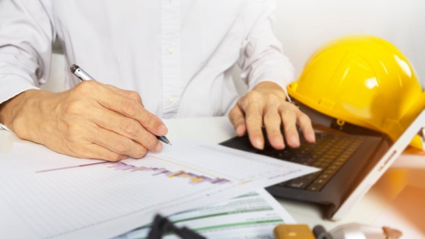 A construction worker does office work. Next to it a helmet.