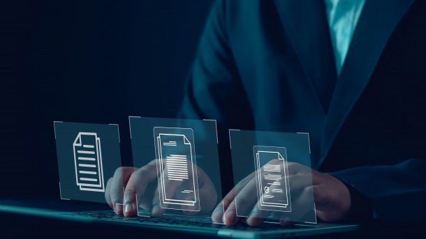 Person an einem Laptop. Darüber Projektionen von Dokumentensymbolen