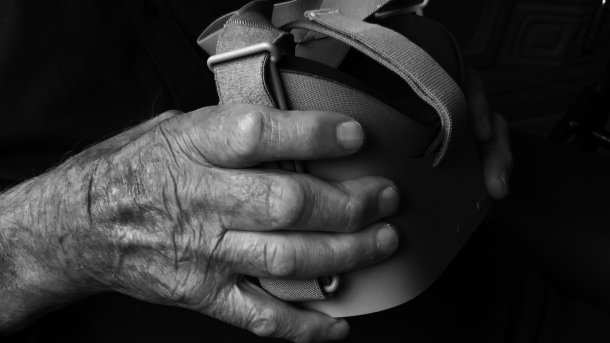 A wrinkled hand holds VR glasses.