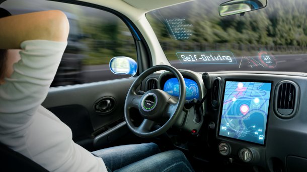 View inside a self-driving car, the driver has his hands behind his head