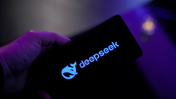 A black cell phone screen in one hand, with the words "deepseek" written on it in blue.