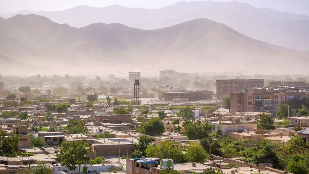 Flat houses among trees, dust clouds, and mountains in the background