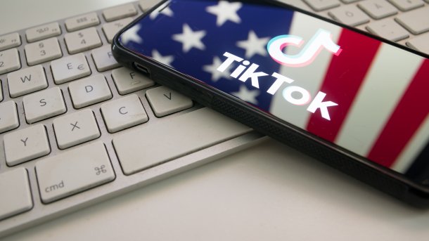 A smartphone on a keyboard, with the US flag reflected in the display featuring the TikTok logo. 