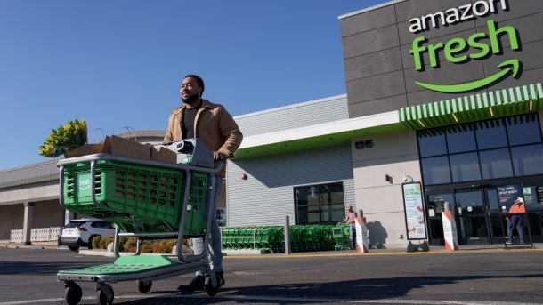 Ein Mann mit einem Einkaufswagen kommt aus einem Supermarkt, über dessen Eingang ein "Amazon Fresh" Schild hängt.