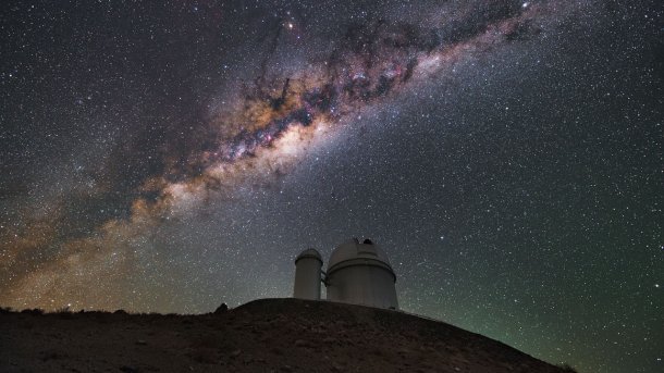 Telescope on a mountain, above it the starry sky, the band of the Milky Way clearly visible.