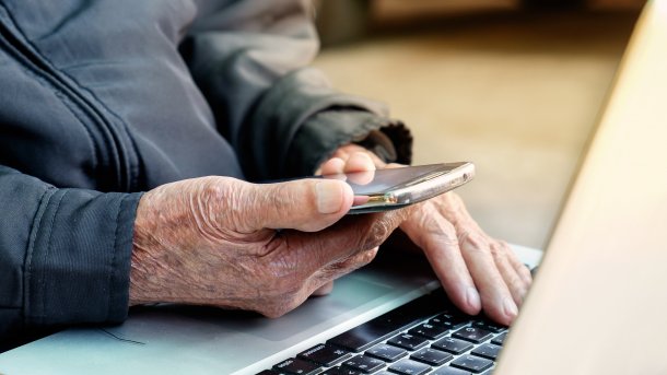 Elderly person at smartphone in front of laptop