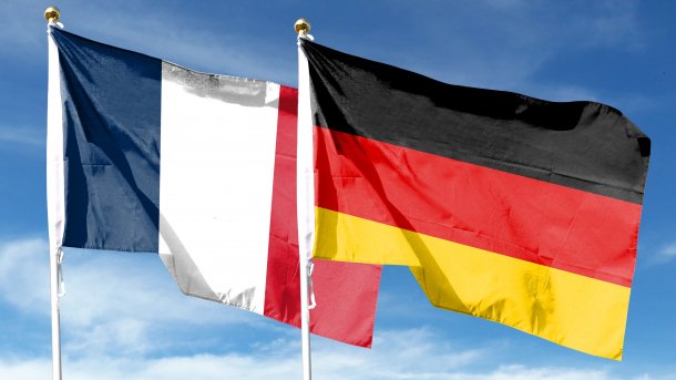 Die Flaggen Frankreichs und Deutschlands vor einem leicht bewölkten blauen Himmel.