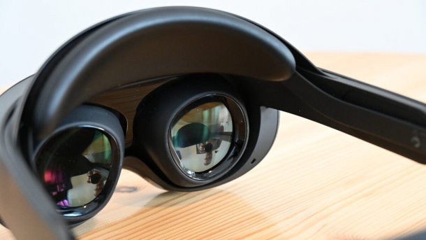 Der Blick auf die Linsen einer schwarzen VR-Brille, die auf einem hellen Holztisch liegt.