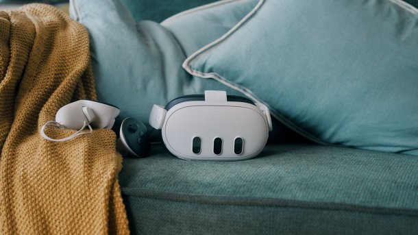 Meta Quest samt Controller liegt auf einer dunkelgrünen Couch.