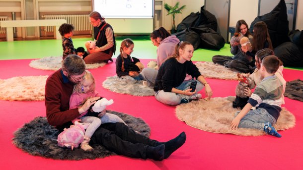 Kinder und Erwachsene sitzen in einem Raum und streicheln Roboter-Meerschweinchen.