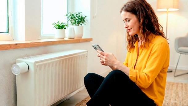 Frau mit iPhone vor einem Heizkörper sitzend.