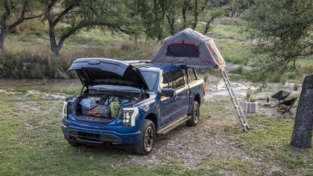 Camping scene: Blue Ford F150 Lightning with a tent on the bed and an open frunk full of stuff