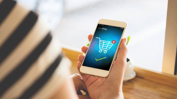 A woman holds a mobile phone, on the screen of which a payment process for an online purchase is visible.