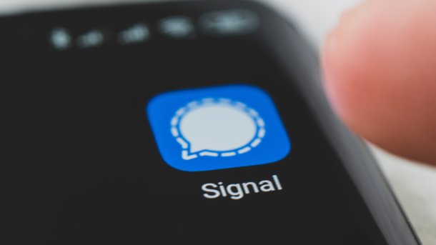Signal-App auf einem Smartphone, darüber eine Fignerspitze