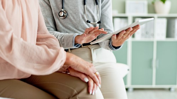 Eine Person hält ein Tablet, daneben eine ältere Person mit einer rosa Bluse.