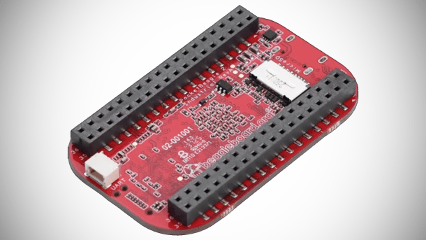 Nahaufnahme eines PocketBeagle 2 Industrial, eines kleinen roten Einplatinencomputers mit zwei Reihen schwarzer Stiftleistenbuchsen, einem weißen Anschluss für UART und klar erkennbaren Leiterbahnen und Bauteilen auf der Oberseite.