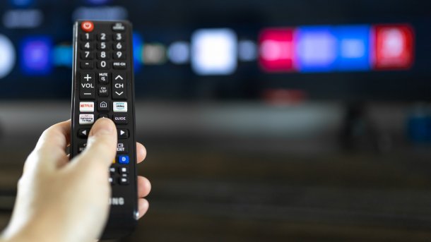 Hand hält Samsung-Fernbedienung vor Smart-TV-Homescreen.