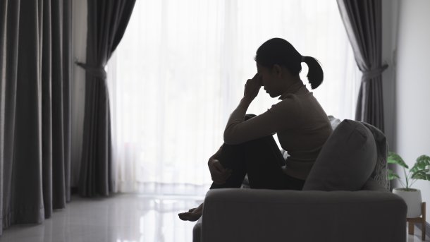 Mädchen versteckt Kopf in den Armen und hält Smartphone.