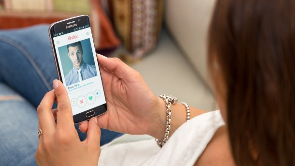 Woman with smartphone in hand, on which a man's profile is open in Tinder.