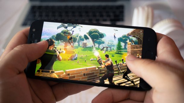 Two hands holding a smartphone and playing Fortnite on it.