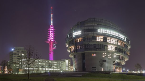 Der in Pink angestrahlte Antennenturm "Telemax" der Deutschen Telekom in Hannover bei Nacht mit dem Gebäude des International Neuroscience Institute im Vordergrung.