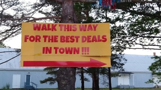 Schild an Baum: "Walk this way for the best deals in Town!!!"