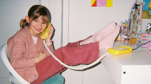 Ein Mädchen nutzt im Kinderzimmer ein Tin-Can-Telefon mit breitem Grinsen.