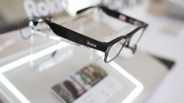 Rokid Smart Glasses on display stand, black frame with integrated technology in the temple, close-up in a blurred environment