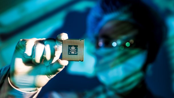 Fab-Mitarbeiter hält Chip zwischen Daumen und Zeigefinger in die Kamera