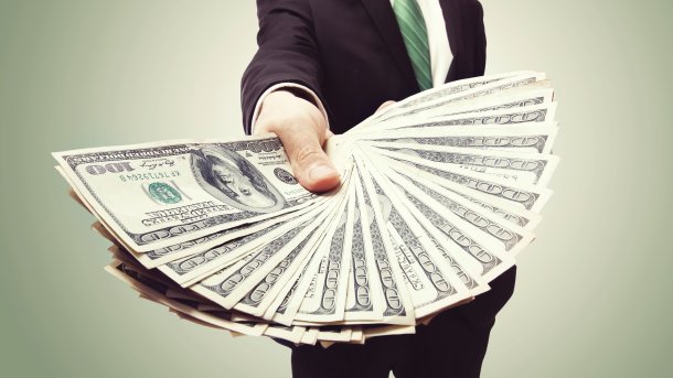 Man in a suit holds fanned-out dollar bills to the camera