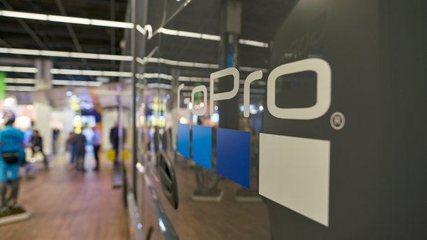 GoPro logo at a trade fair stand; blurred visitors and exhibition areas are visible in the background.