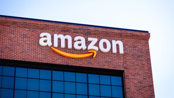 Amazon logo on the facade of a red brick building with large windows below.