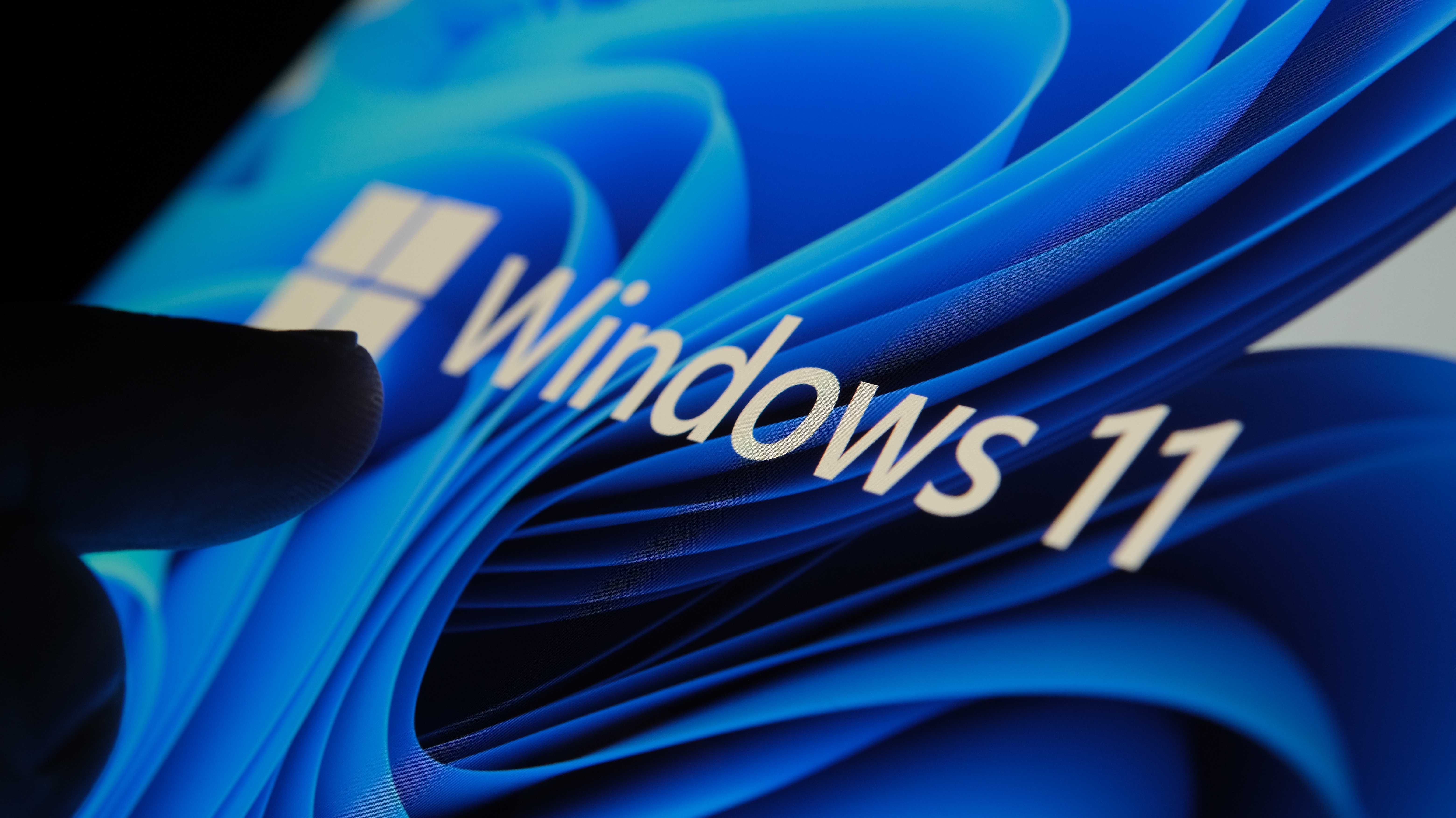 Ein Finger zeigt auf den Windows-11-Startbildschirm. 