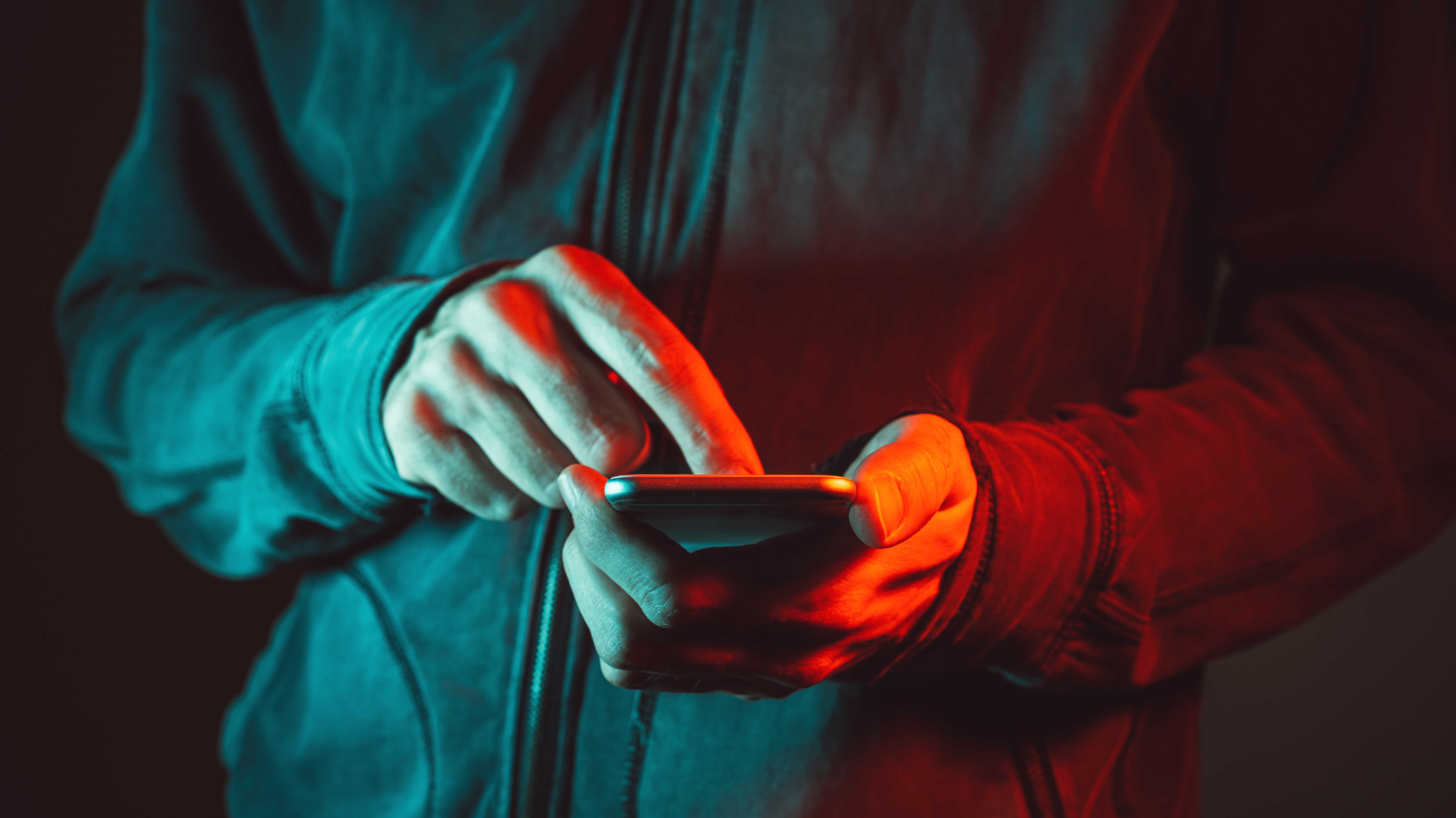 Hände am Smartphone, alles gehüllt in rotes Licht