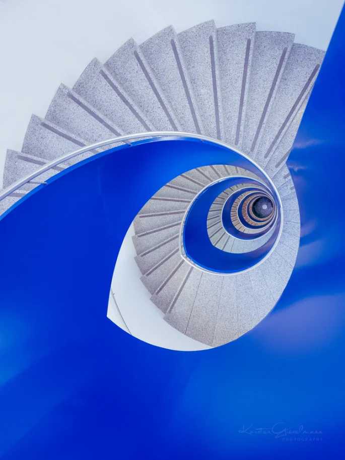 Hellgraue Wendeltreppe mit blauem Geländer von oben